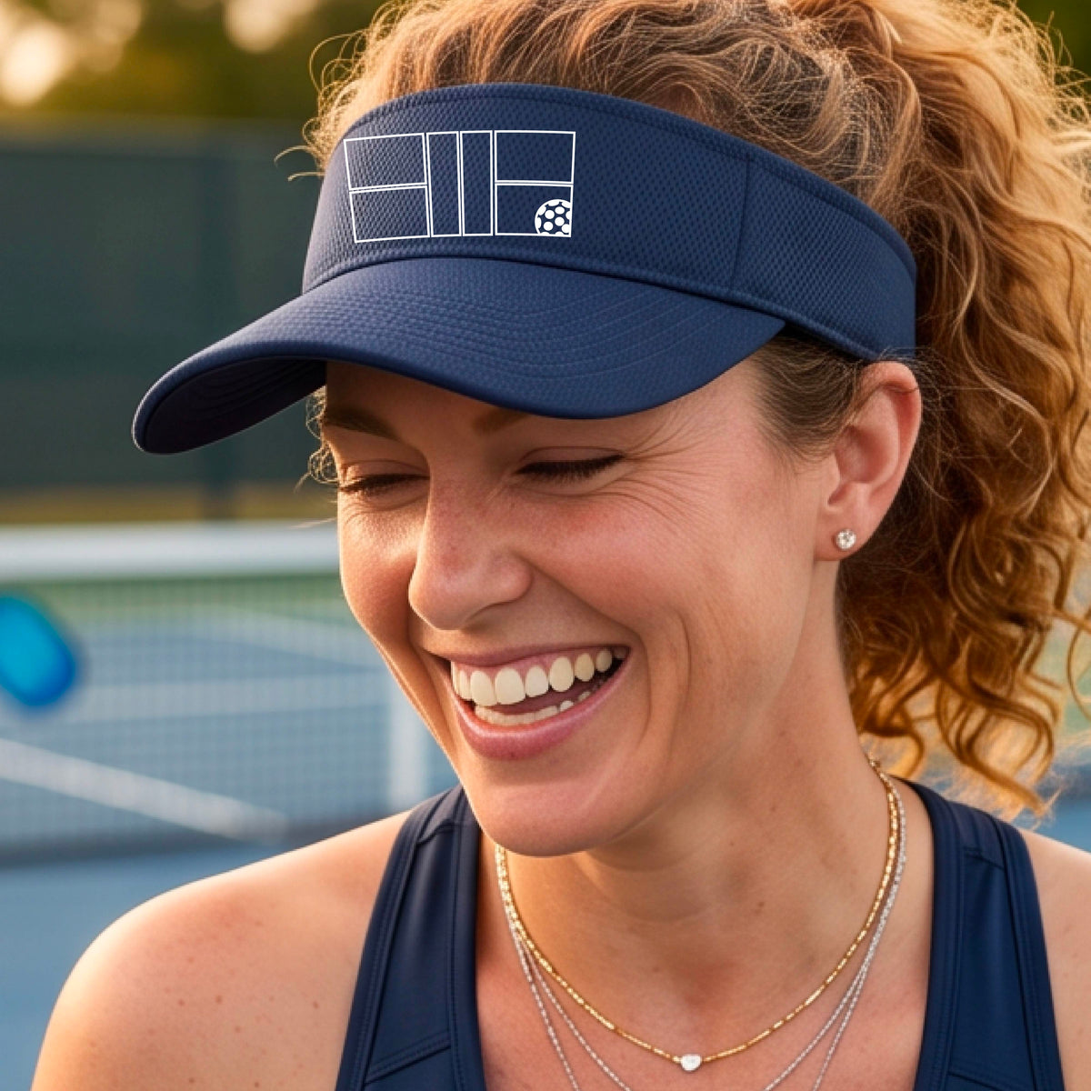 A close up of a navy blue visor with a white pickleball court and ball graphic on the front. 