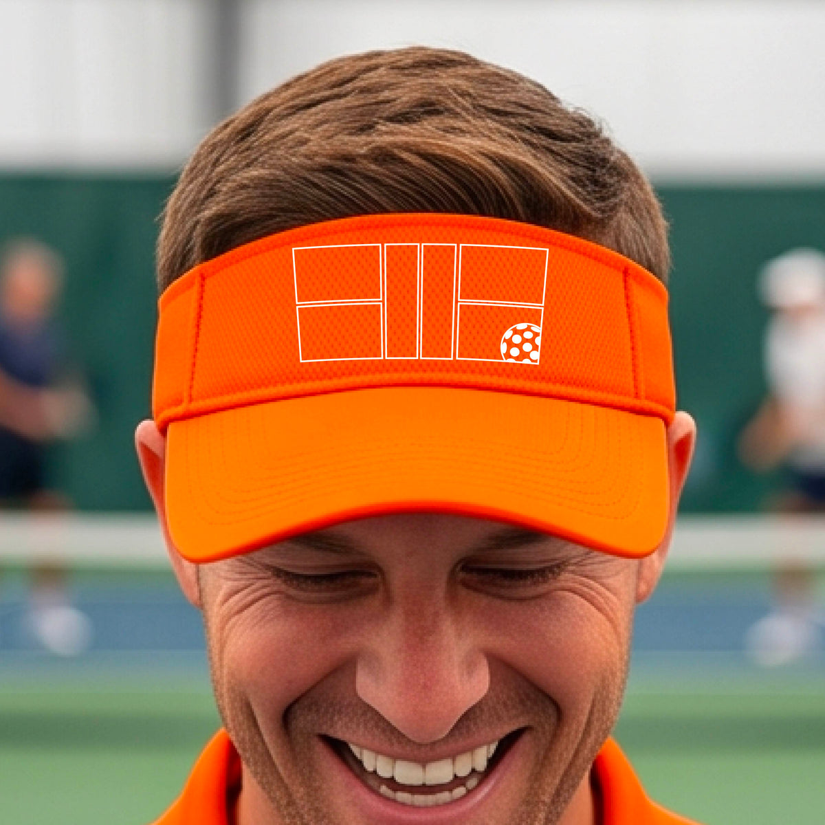 A close up of an orange visor with a white pickleball court and ball graphic on the front. 