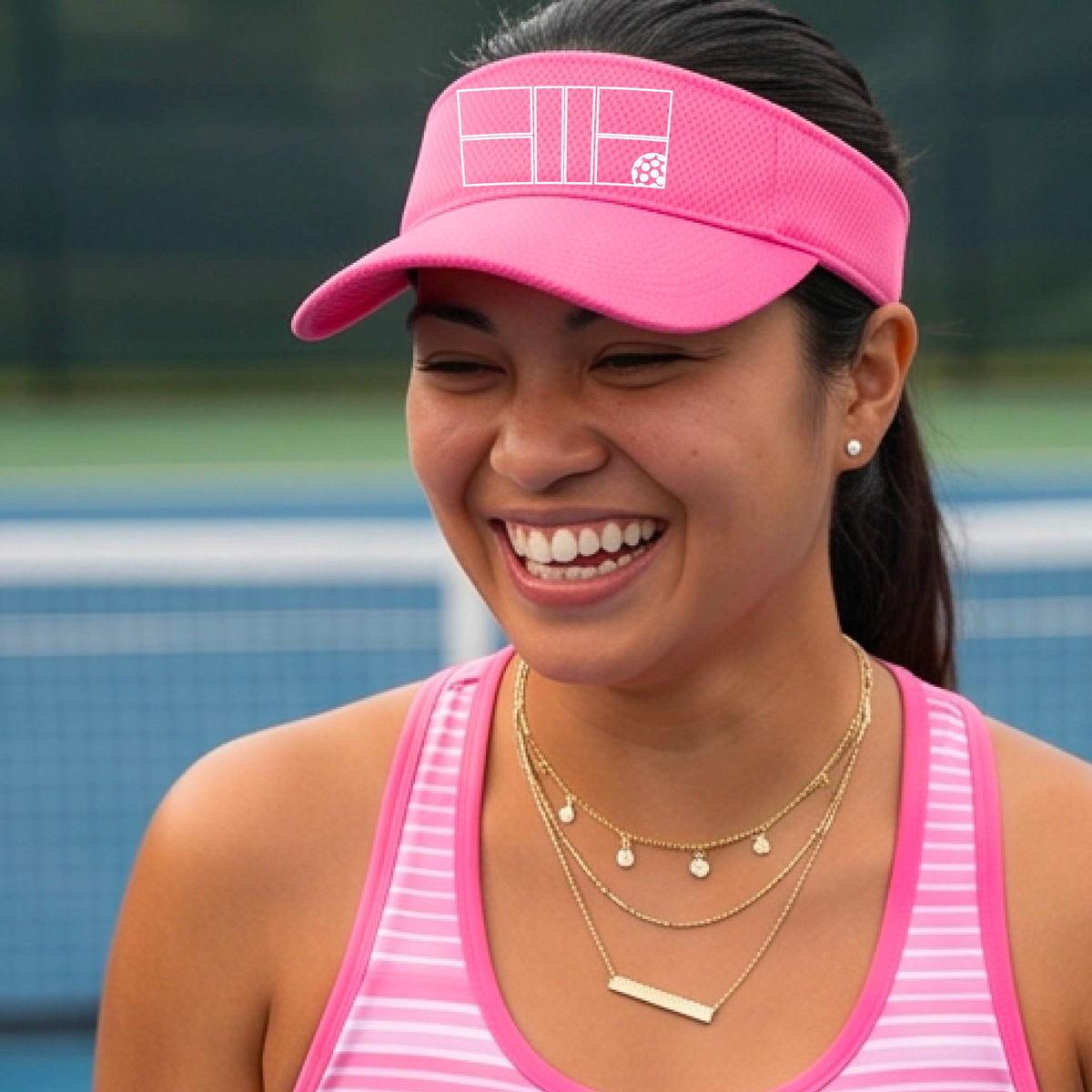 A close up of a pink visor with a white pickleball court and ball graphic on the front. 