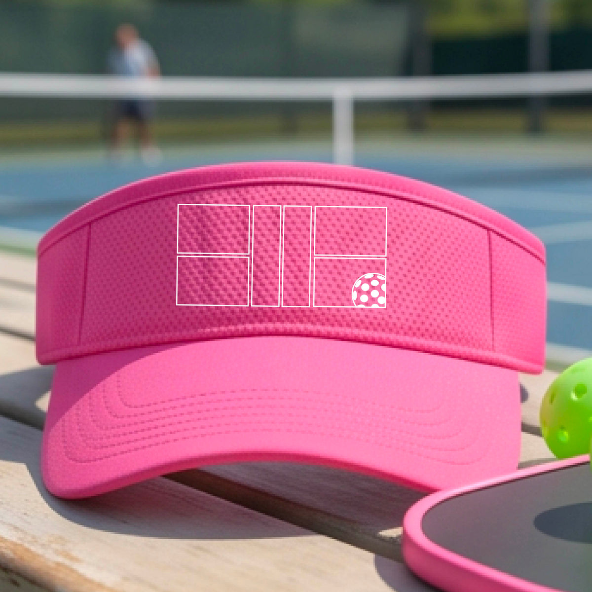 A close up of a pink visor with a white pickleball court and ball graphic on the front. 