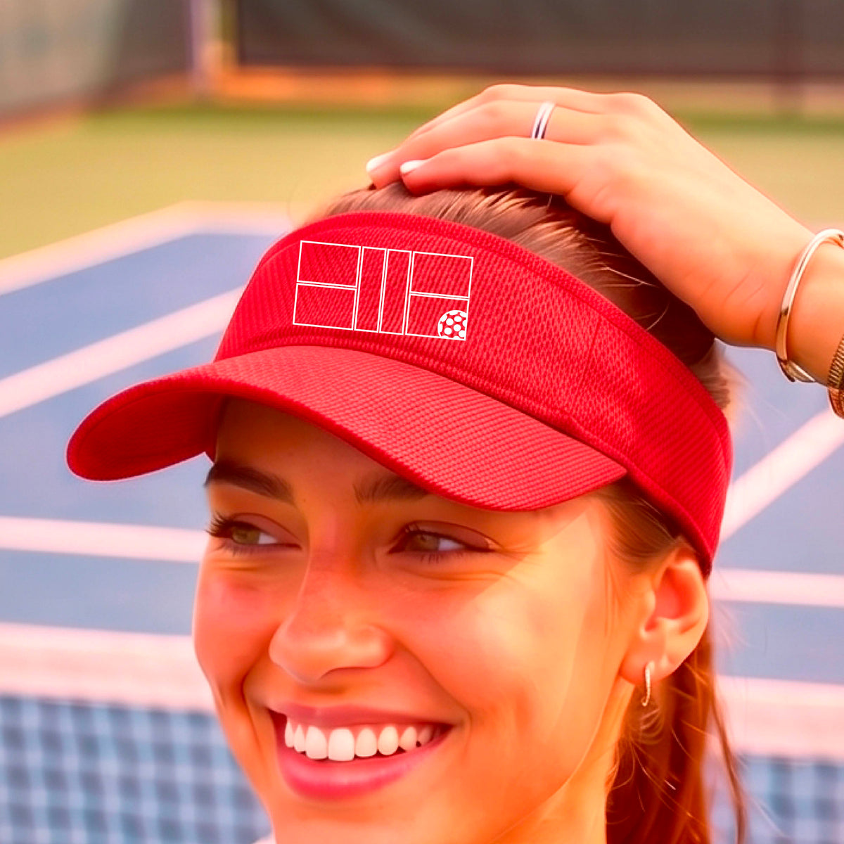 A close up of a red visor with a white pickleball court and ball graphic on the front. 