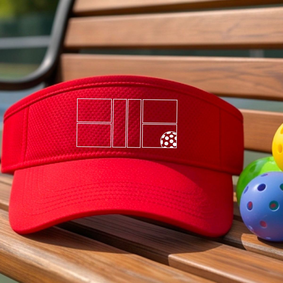 A close up of a red visor with a white pickleball court and ball graphic on the front. 