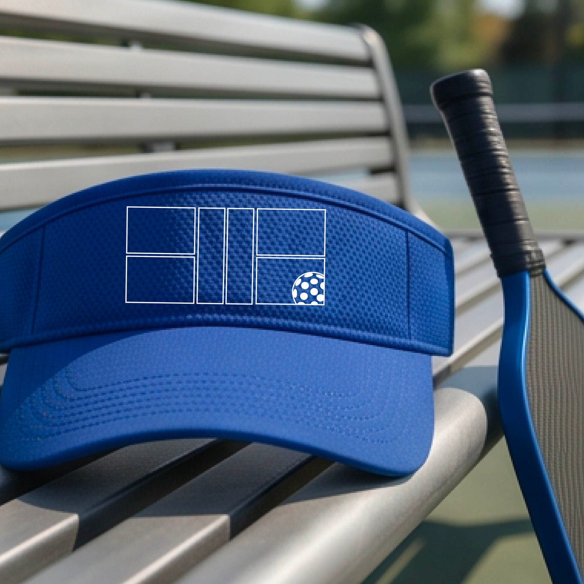 A close up of a royal blue visor with a white pickleball court and ball graphic on the front. 