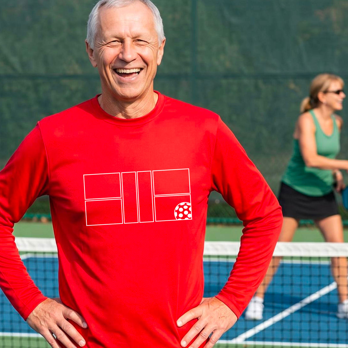 A smiling man wearing a red long-sleeve athletic shirt with a white geometric pickleball court and ball graphic on the chest,.