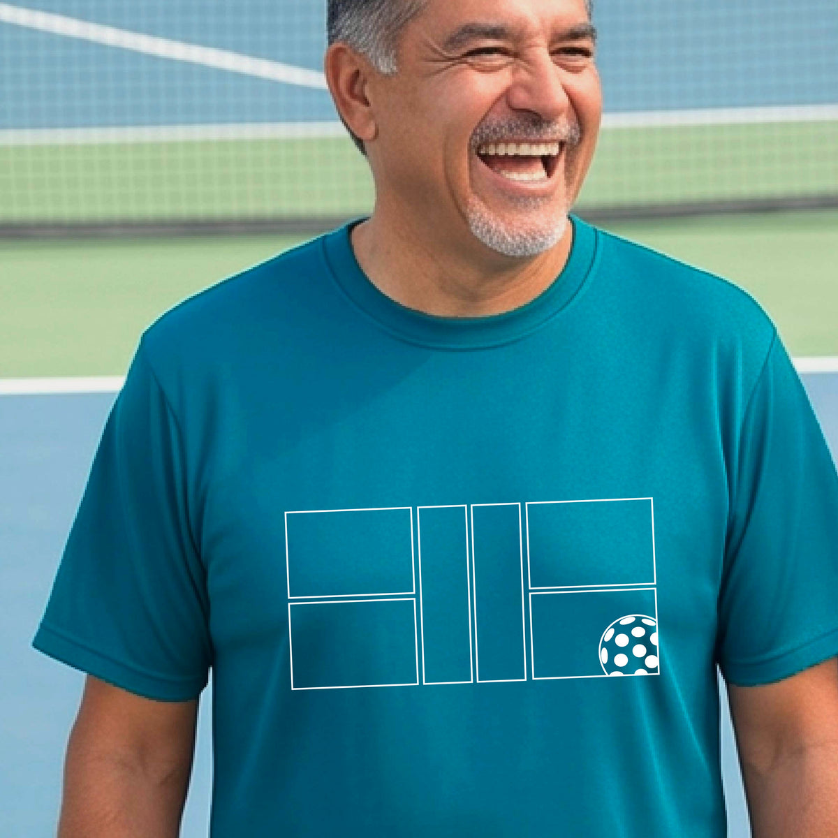 A man wearing a teal short-sleeve shirt with a graphic of a white pickleball court and ball on the front, standing on a pickleball court. 