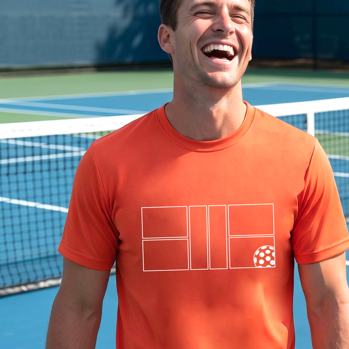 A man wearing an orange short-sleeve shirt with a graphic of a white pickleball court and ball on the front, standing on a pickleball court. 