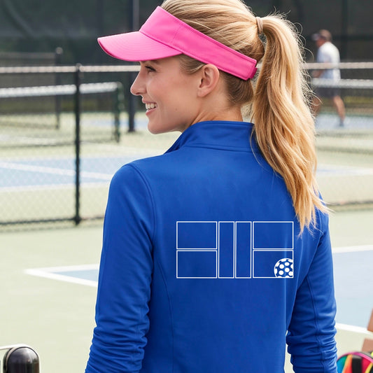 A woman on a pickleball court wearing a bright blue long-sleeve quarter-zip athletic jacket with a white geometric line pickleall court and ball graphic on the back.