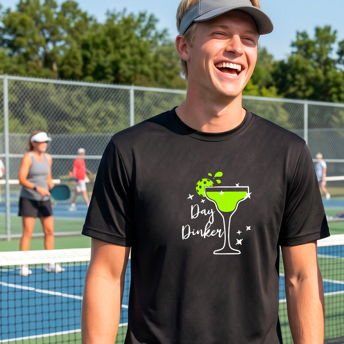 A man laughing on a pickleball court wearing a black t-shirt with a 'Day Dinker' martini with a pickleball lime garnish graphic in green and white.