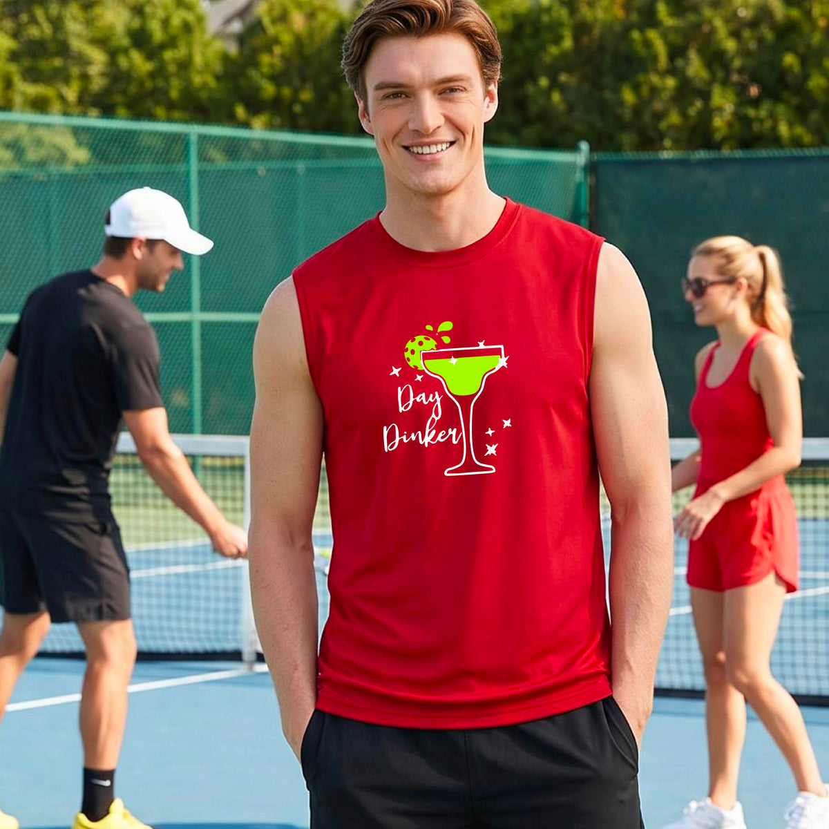 A man smiling on an outdoor pickleball court wearing a red sleeveless tank top with a green cocktail martini glass with a pickleball lim garnish graphic and the words 'Day Dinkster' printed on the front. 