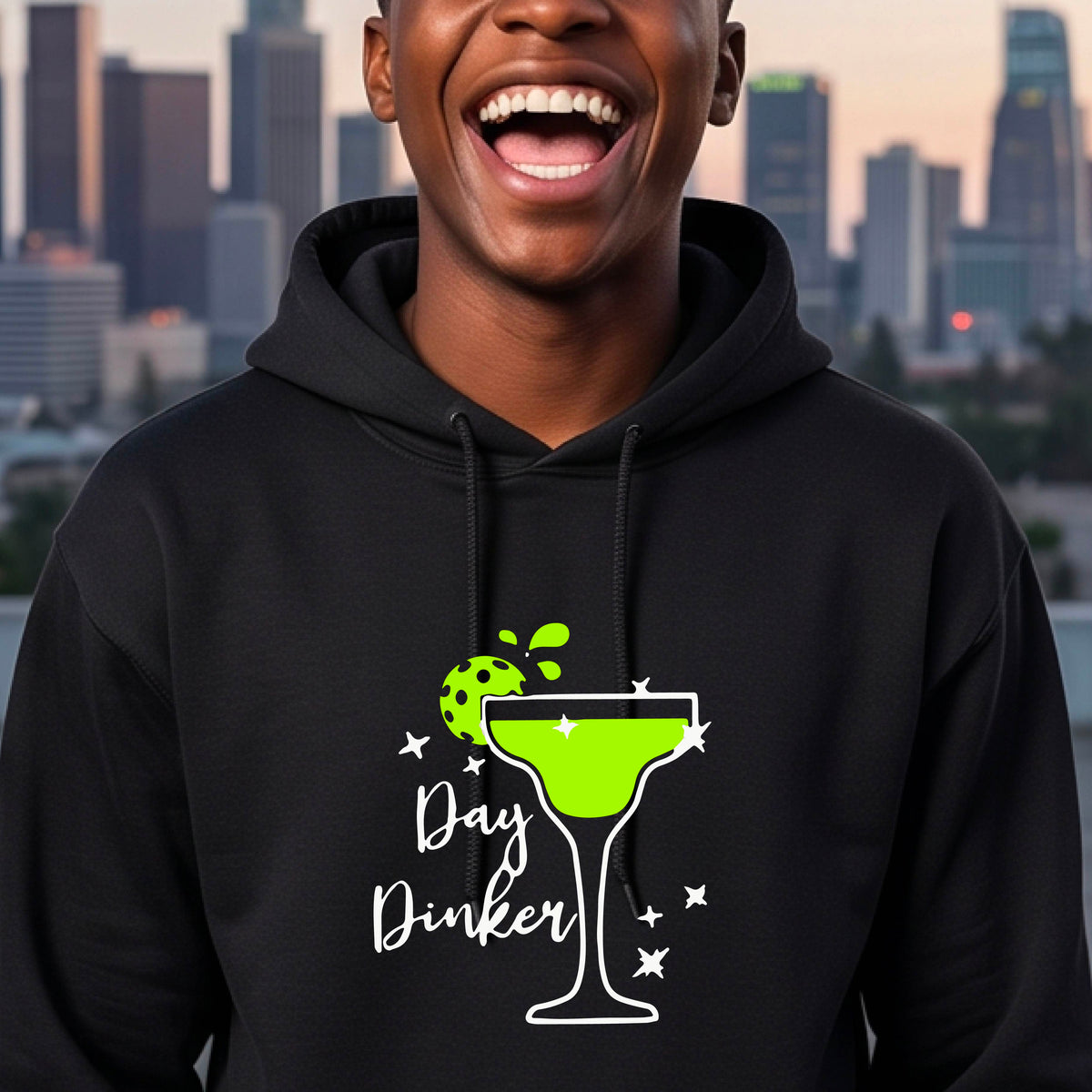 A smiling man wearing a black hoodie with a green margarita glass graphic and green pickleball lime garnish and the words 'Day Dinker' on the front.