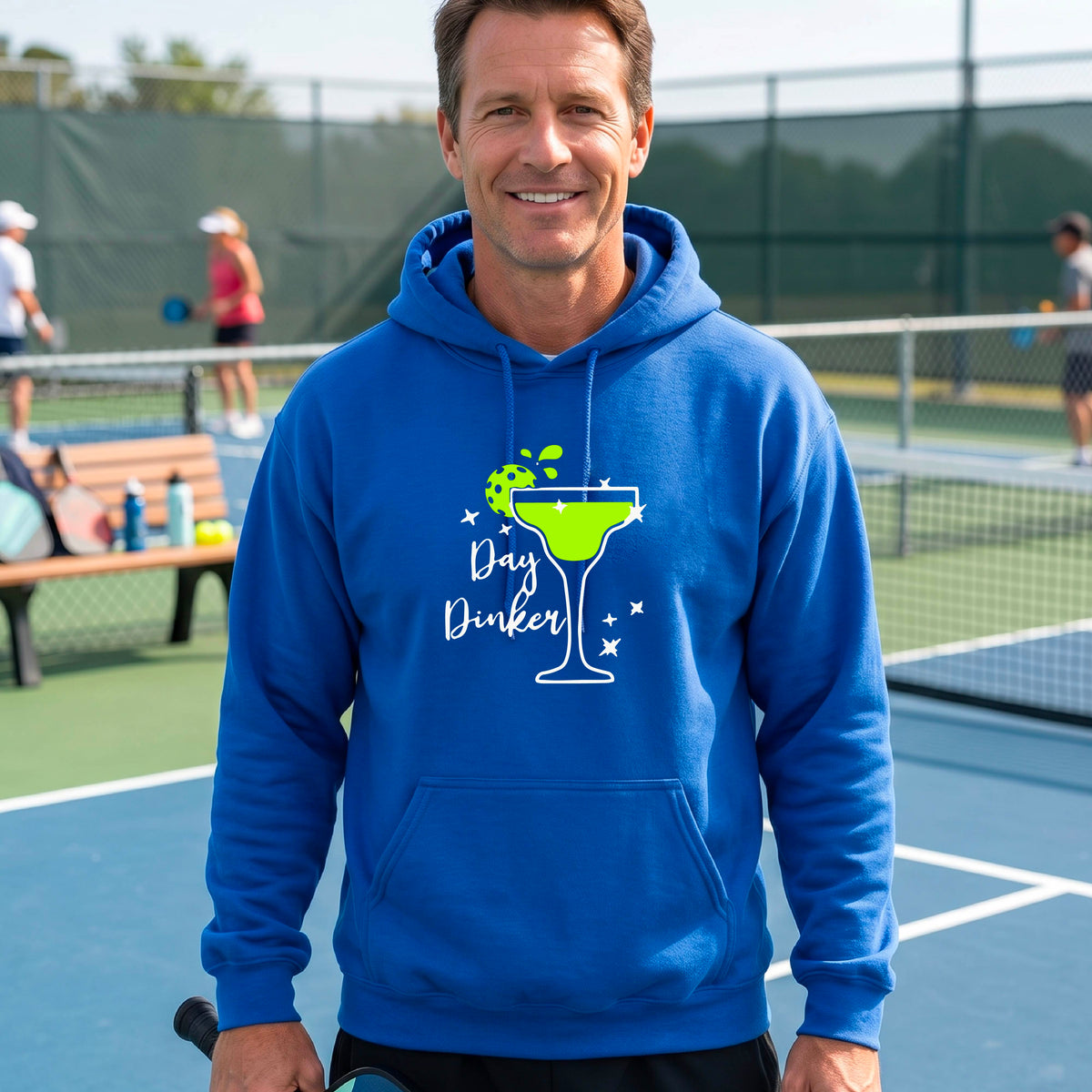 A smiling man wearing a royal blue hoodie with a green margarita glass graphic and green pickleball lime garnish and the words 'Day Dinker' on the front.