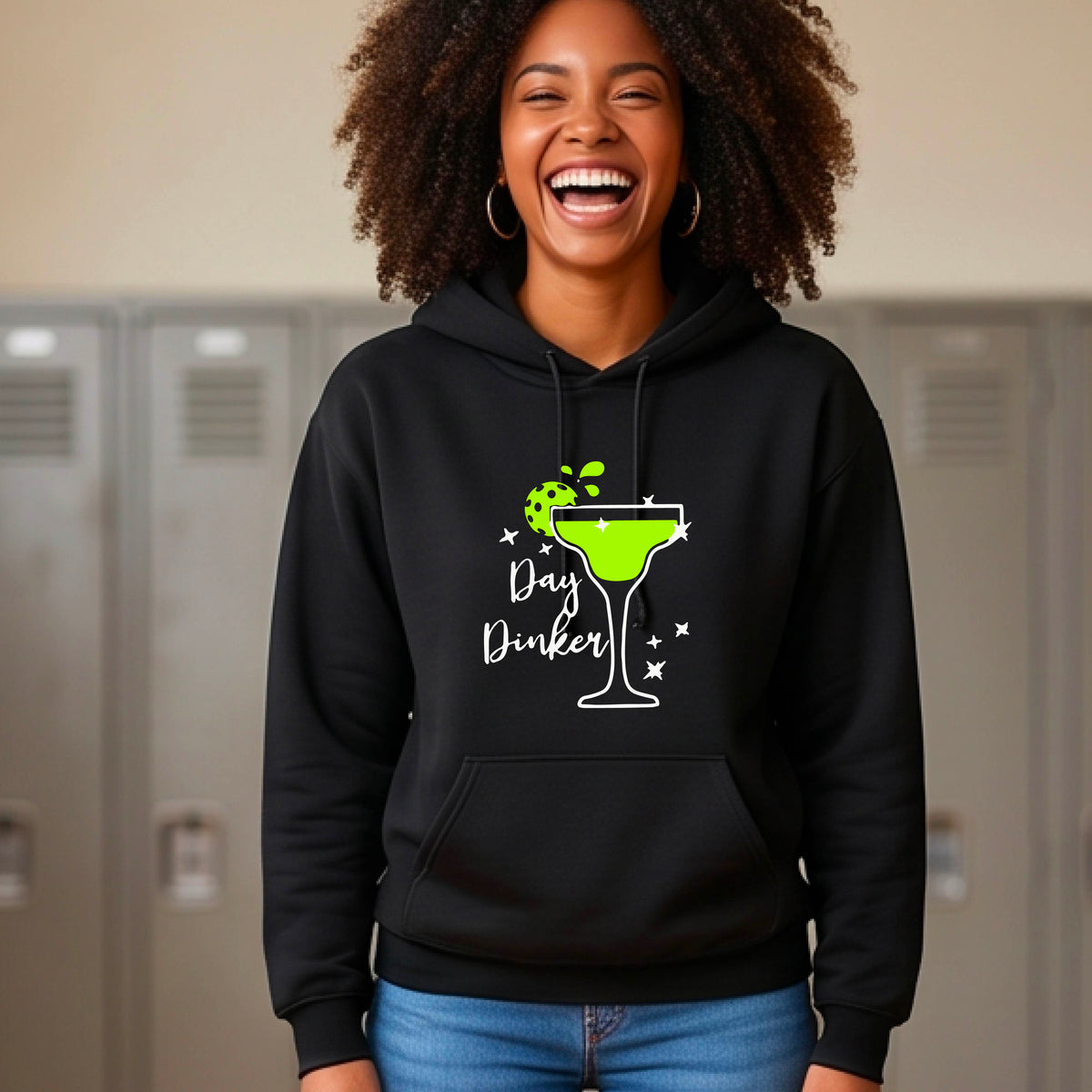 A smiling woman wearing a black hoodie with a green margarita glass graphic and green pickleball lime garnish and the words 'Day Dinker' on the front.
