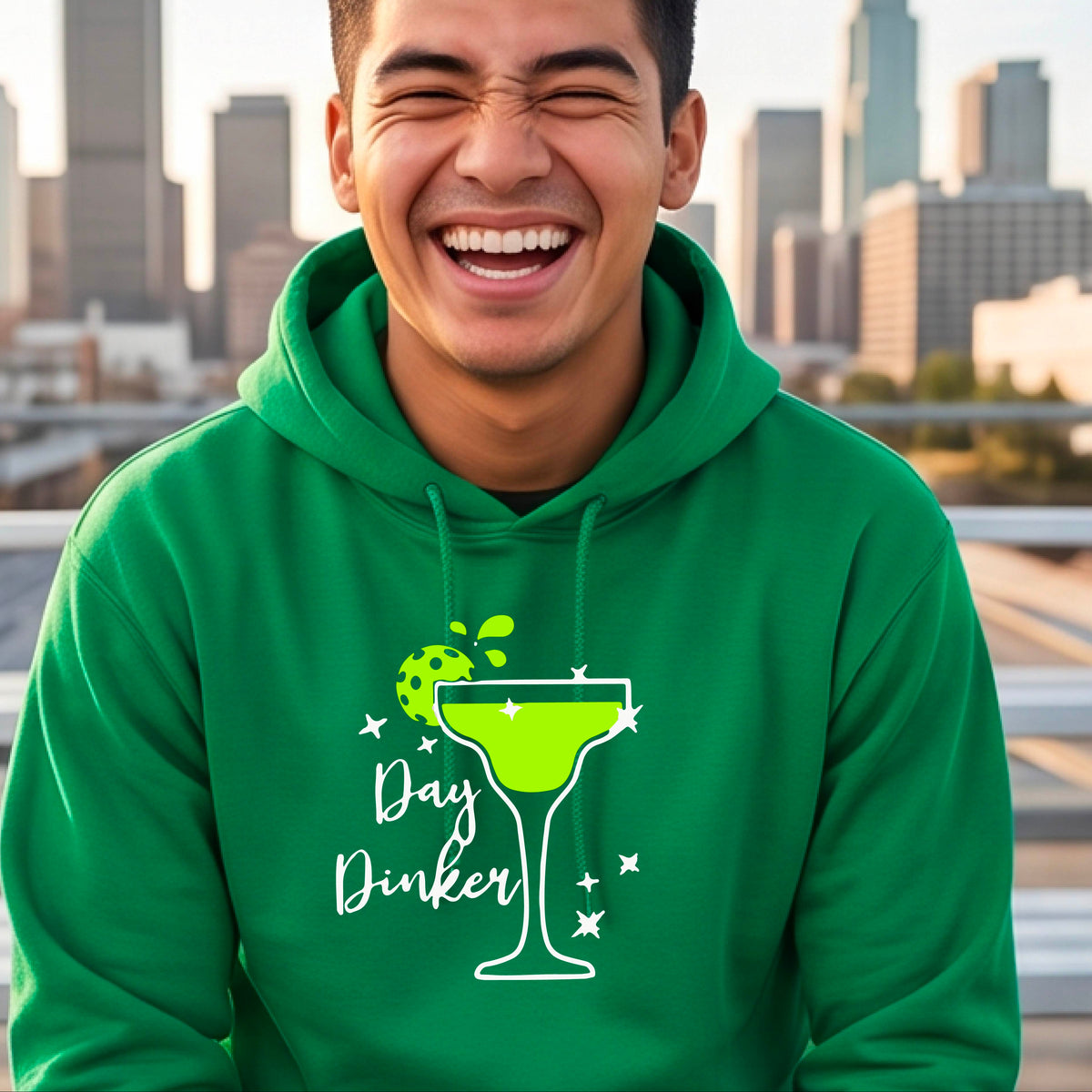 A smiling man wearing a green hoodie with a green margarita glass graphic and green pickleball lime garnish and the words 'Day Dinker' on the front.