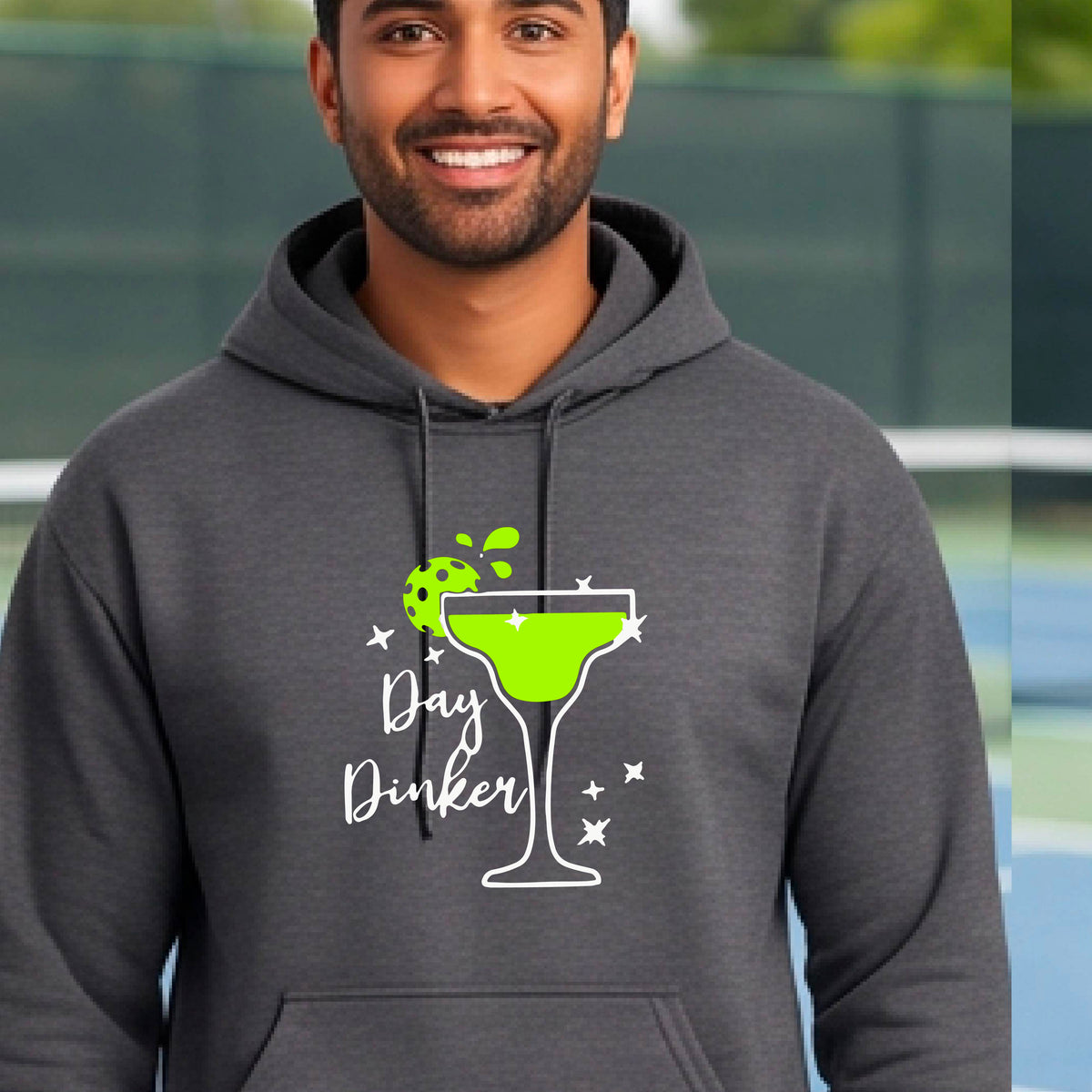 A smiling man wearing a gray hoodie with a green margarita glass graphic and green pickleball lime garnish and the words 'Day Dinker' on the front.