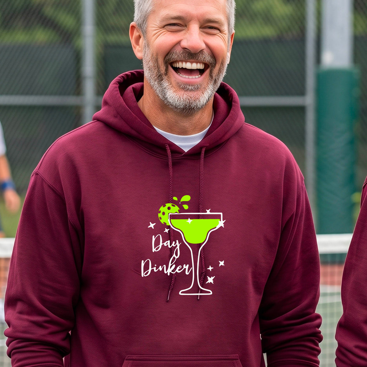 A smiling man wearing a maroon hoodie with a green margarita glass graphic and green pickleball lime garnish and the words 'Day Dinker' on the front.