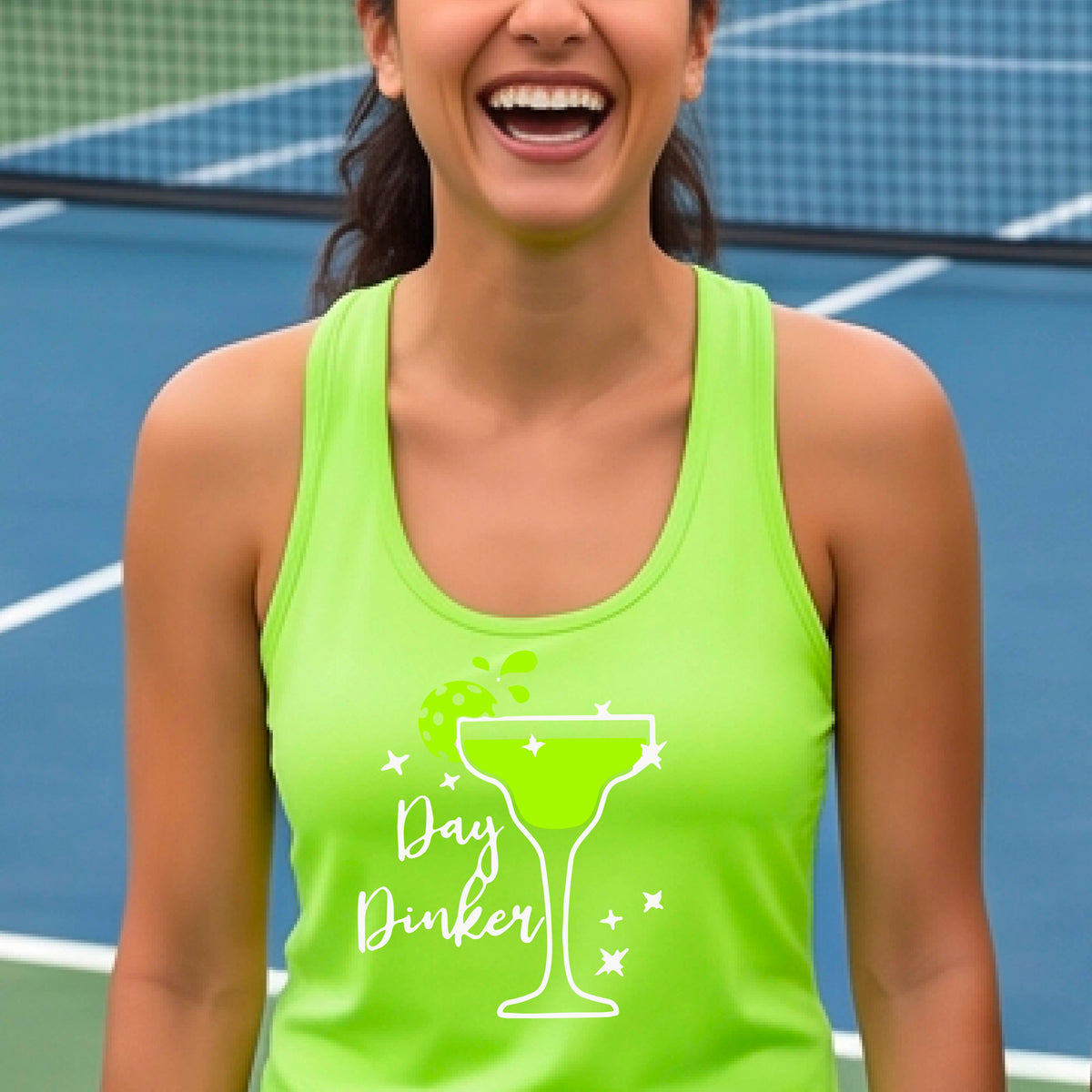 A woman on a pickleball court wearing a lime green racerback tank top with a 'Day Dinker' graphic featuring a green margarita glass, pickleball lime garnish and white script text.
