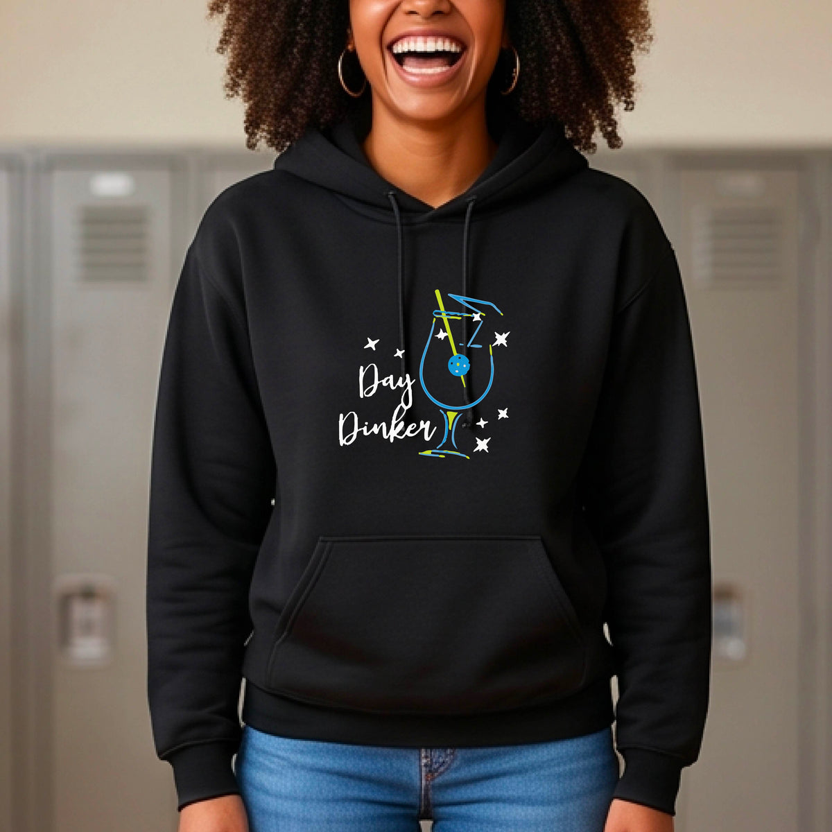 A man wearing a black hoodie with a colorful graphic on the chest that reads 'Day Dinker' alongside a martini cocktail glass with a pickelball olive garnish illustration.