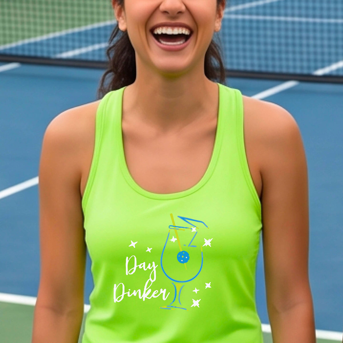 A woman wearing a lime green athletic tank top with a colorful 'Day Dinker' martini cocktail graphic with a pickleball olive as a garnish. on the front, standing on a pickleball court.