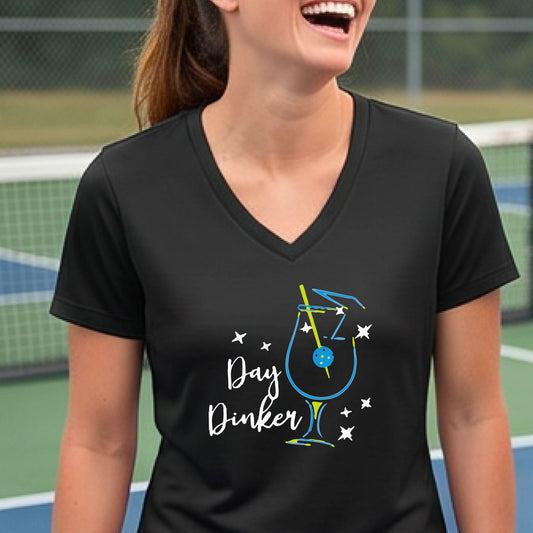 A woman wearing a black V-neck t-shirt with a colorful 'Day Dinker' martinin cocktail graphic with a pickleball garnish on the front.