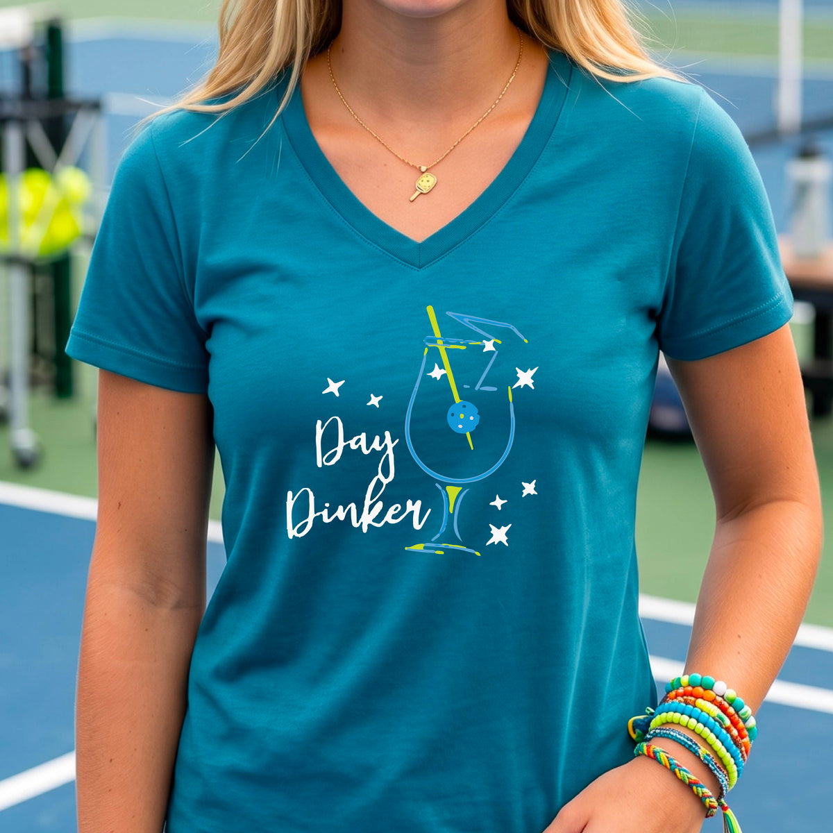 A woman wearing a teal V-neck t-shirt with a colorful 'Day Dinker' martinin cocktail graphic with a pickleball garnish on the front.