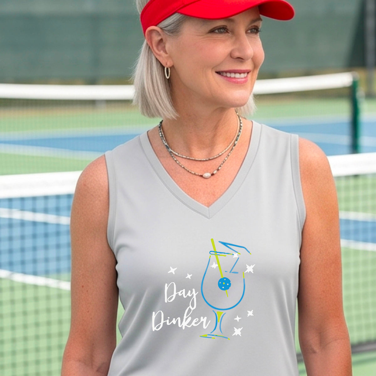 A woman wearing a light gray sleeveless V-neck athletic tank top with a colorful cocktail martini glass with a pickleball olive garnish"