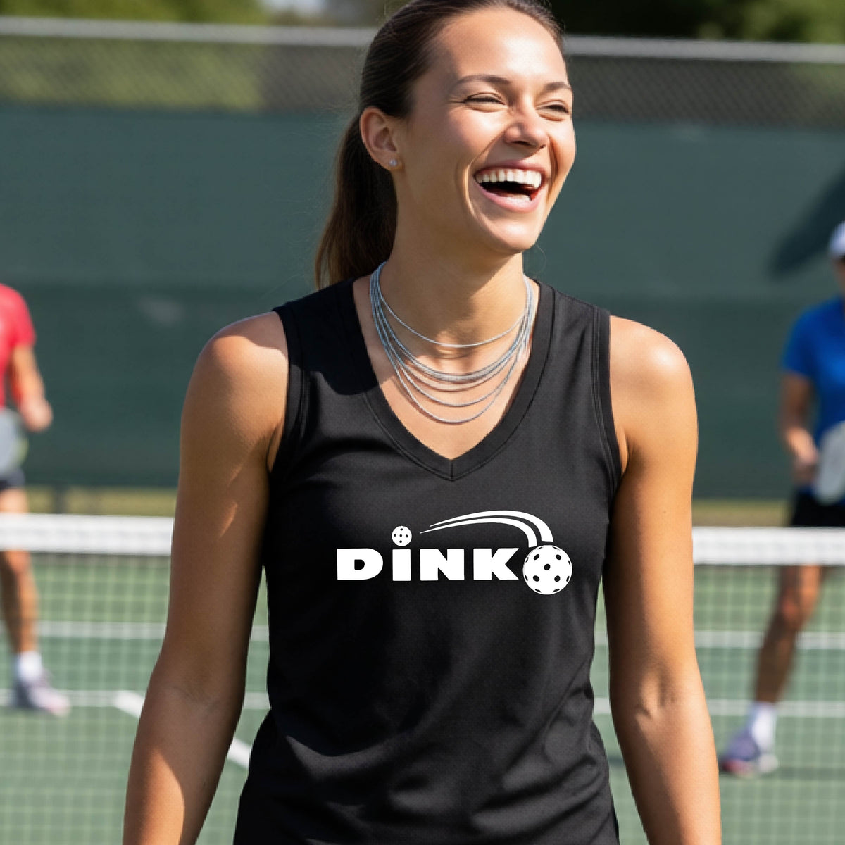 A woman laughing on an outdoor pickleball court wearing a black sleeveless tank top with a white 'DINK' graphic and a pickleball in flight over the text.