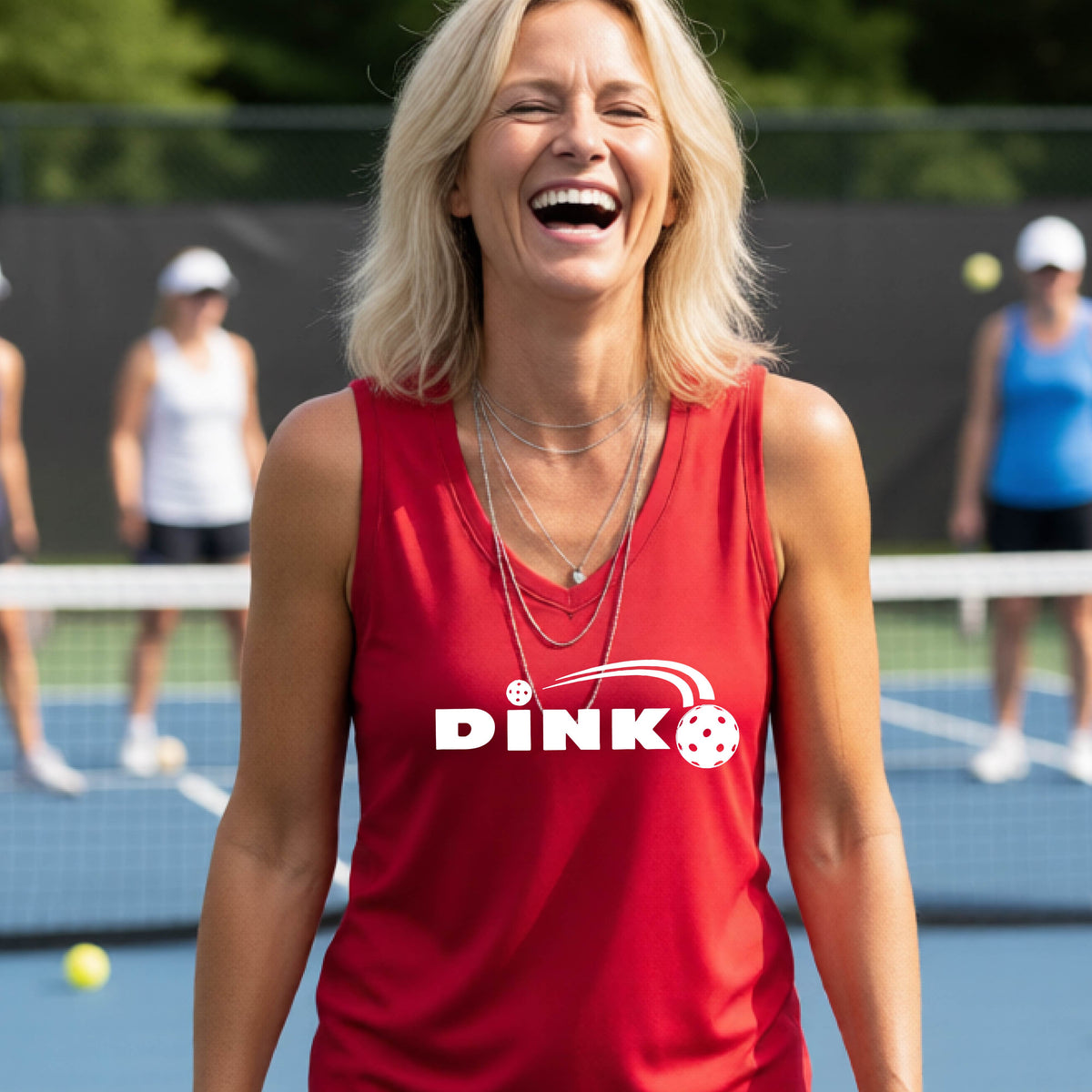 A woman laughing on an outdoor pickleball court wearing a red sleeveless tank top with a white 'DINK' graphic and a pickleball in flight over the text.