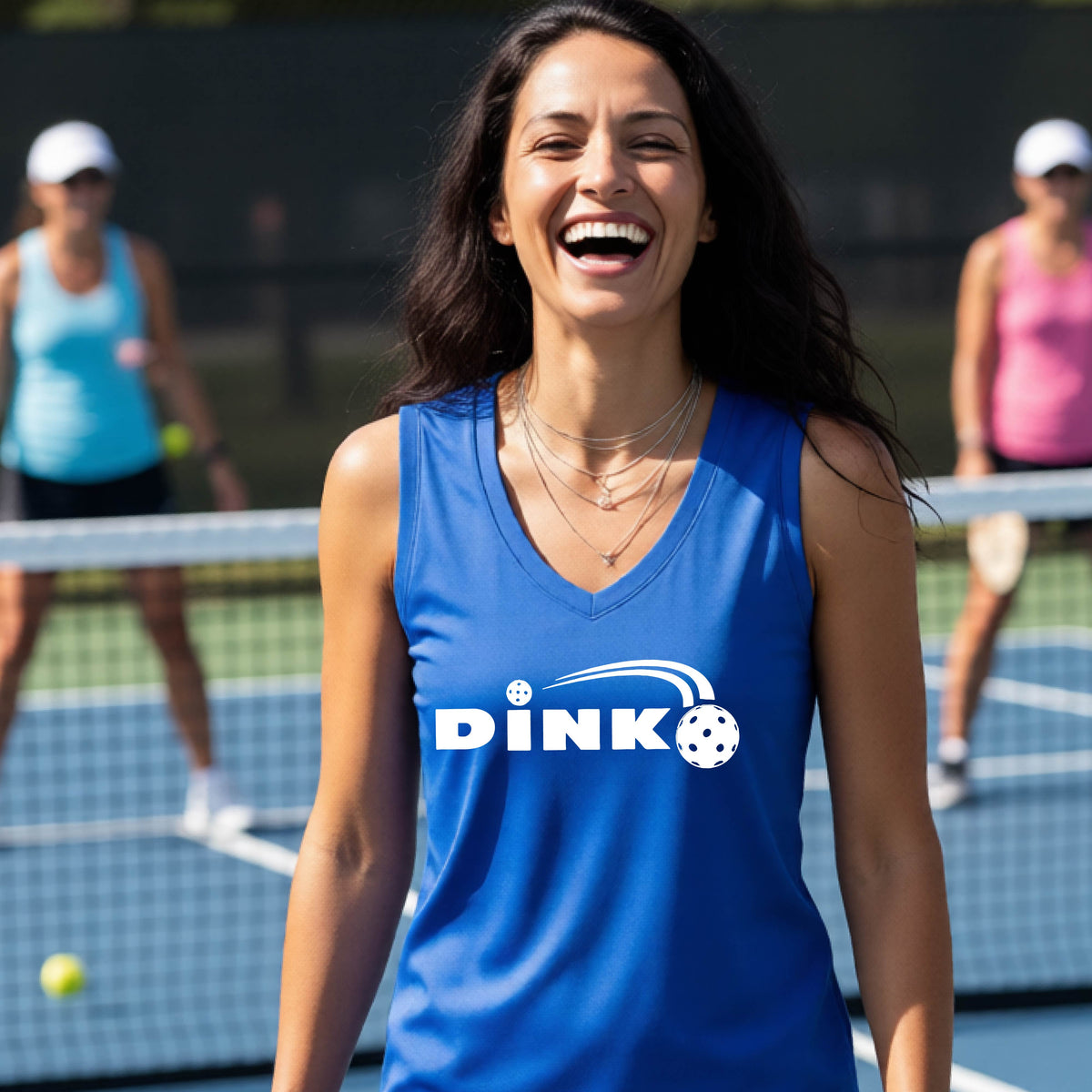 A woman laughing on an outdoor pickleball court wearing a royal blue sleeveless tank top with a white 'DINK' graphic and a pickleball in flight over the text.