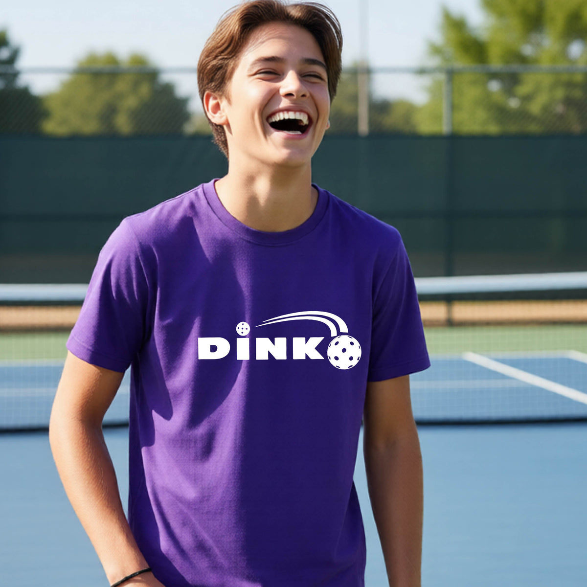 A young person wearing a purple short-sleeve t-shirt with a pickleball design of text 'DINK' with a white pickleall in flight, standing on a pickleball court.