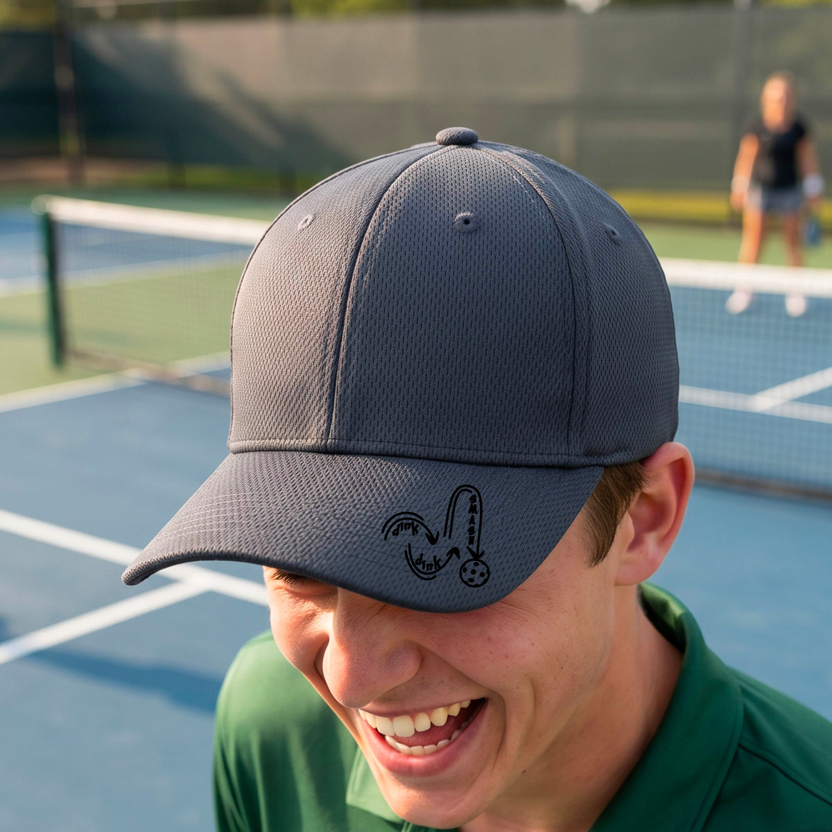 A close-up lifestyle shot of a gray athletic hat with a black pickleball 'DINK DINK SMASH' logo with a pickleball graphic