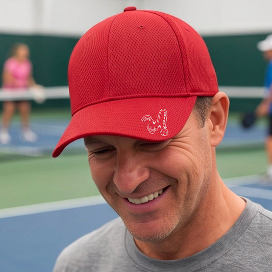 A close-up lifestyle shot of a red athletic mid-profile hat with a white pickleball 'DINK DINK SMASH' logo with a pickleball graphic