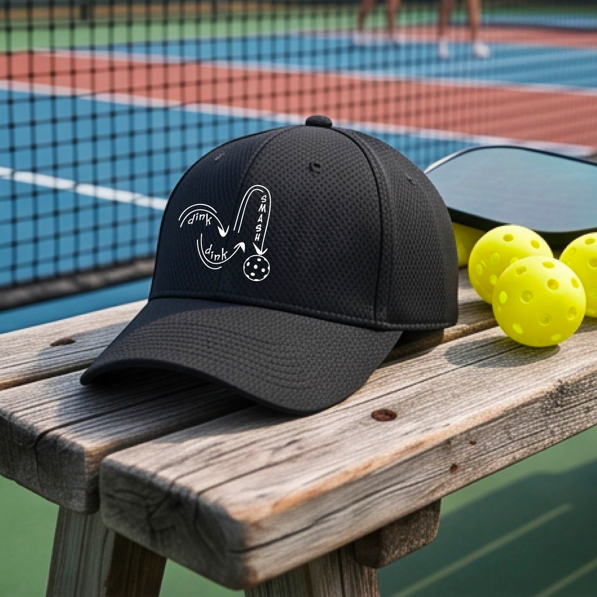 A close-up lifestyle shot of a black athletic mid-profile hat with a white pickleball 'DINK DINK SMASH' logo with a pickleball graphic