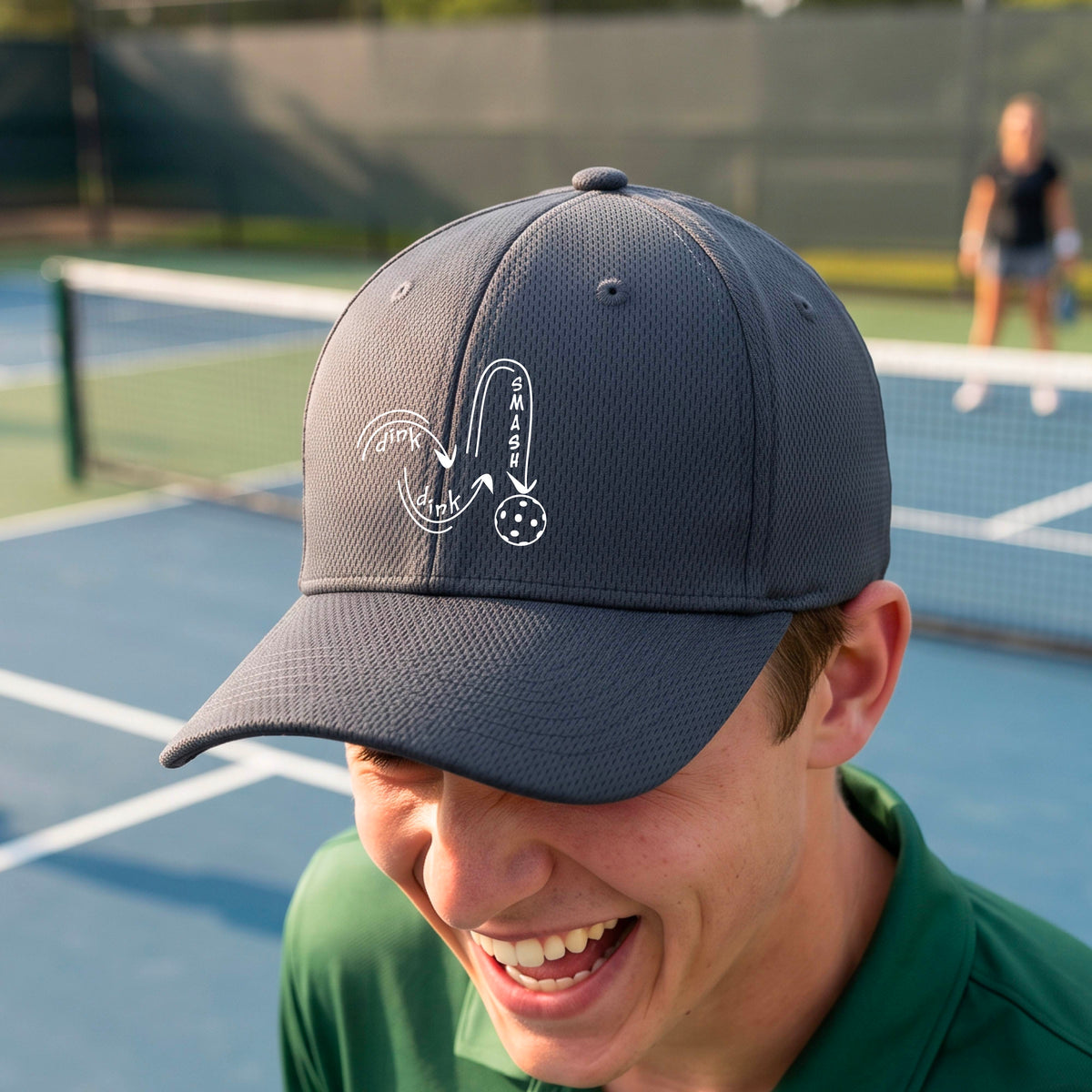A close-up lifestyle shot of a gray athletic mid-profile hat with a white pickleball 'DINK DINK SMASH' logo with a pickleball graphic