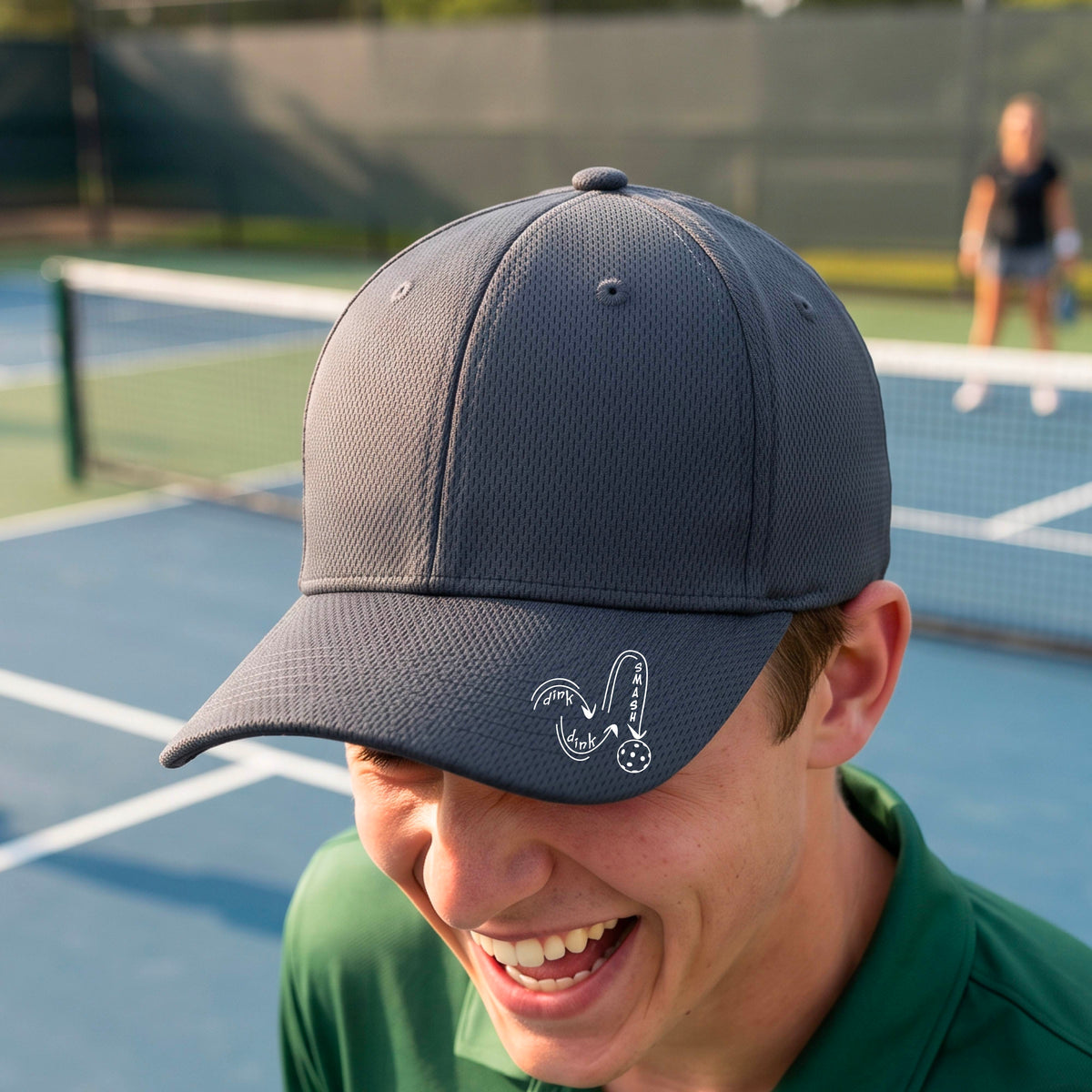 A close-up lifestyle shot of a gray athletic mid-profile hat with a white pickleball 'DINK DINK SMASH' logo with a pickleball graphic