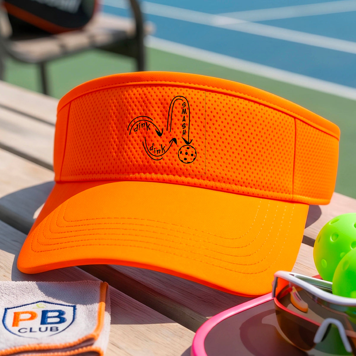 A close-up lifestyle shot of an orange athletic visor with a black pickleball 'DINK DINK SMASH' logo with a pickleball graphic.