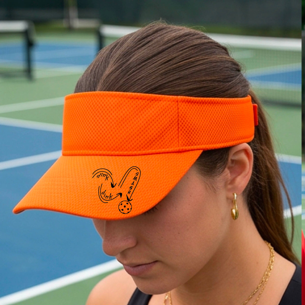 A close-up lifestyle shot of an orange athletic visor with a black pickleball 'DINK DINK SMASH' logo with a pickleball graphic.