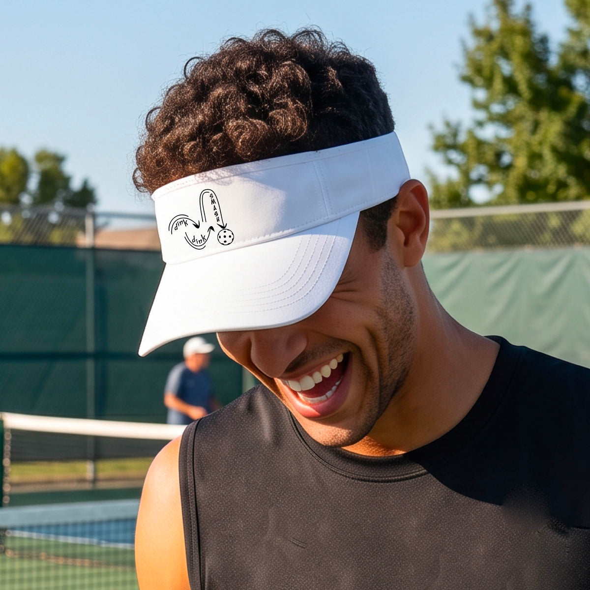 A close-up lifestyle shot of a white athletic visor with a black pickleball 'DINK DINK SMASH' logo with a pickleball graphic.