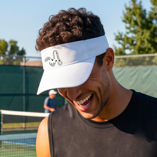 A close-up lifestyle shot of a white athletic visor with a black pickleball 'DINK DINK SMASH' logo with a pickleball graphic.