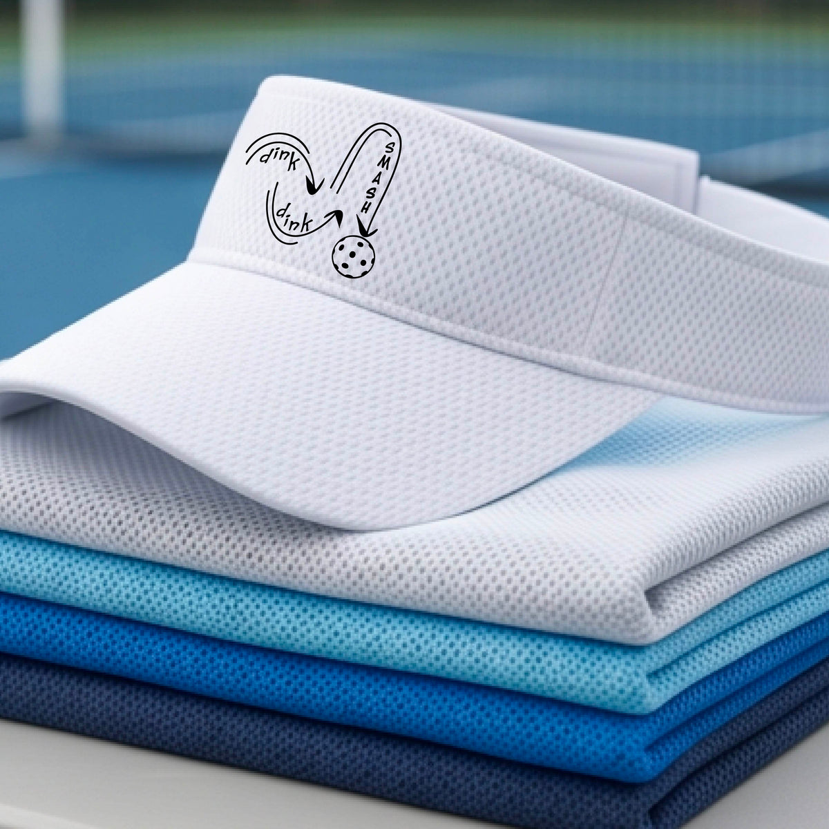 A close-up lifestyle shot of a white athletic visor with a black pickleball 'DINK DINK SMASH' logo with a pickleball graphic.