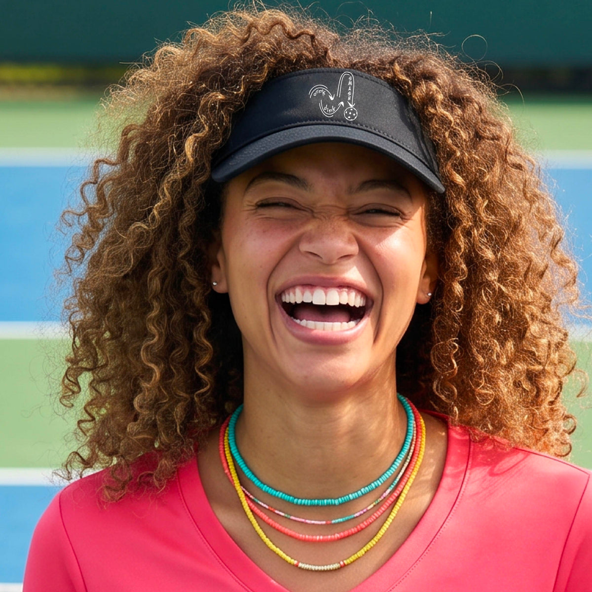 A close-up lifestyle shot of a black athletic visor with a white pickleball 'DINK DINK SMASH' logo with a pickleball graphic