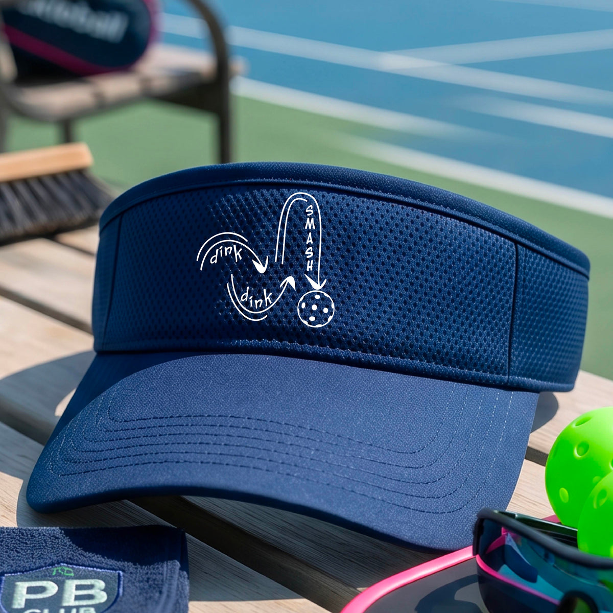 A close-up lifestyle shot of a bright blue athletic visor with a white pickleball 'DINK DINK SMASH' logo with a pickleball graphic