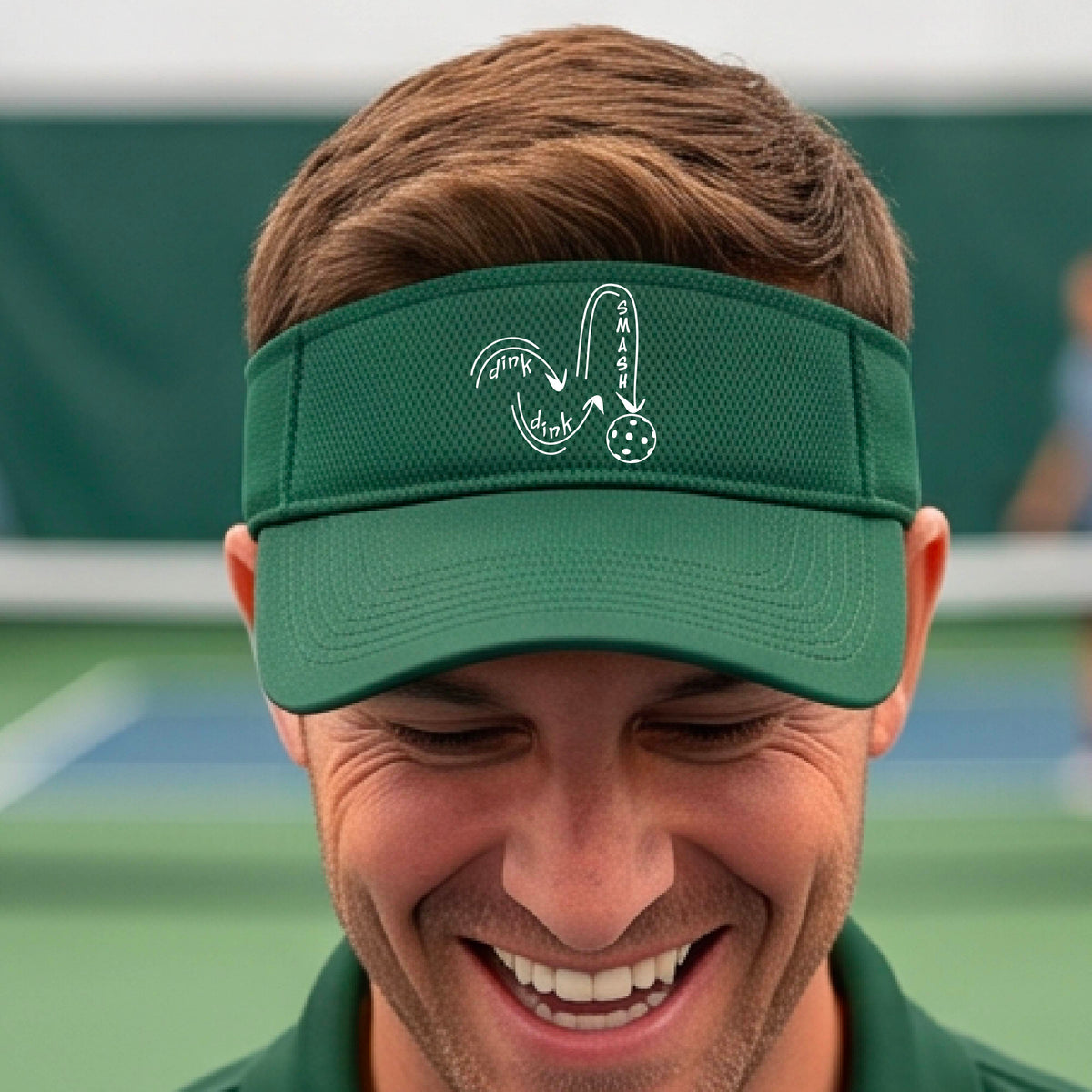 A close-up lifestyle shot of a green athletic visor with a white pickleball 'DINK DINK SMASH' logo with a pickleball graphic