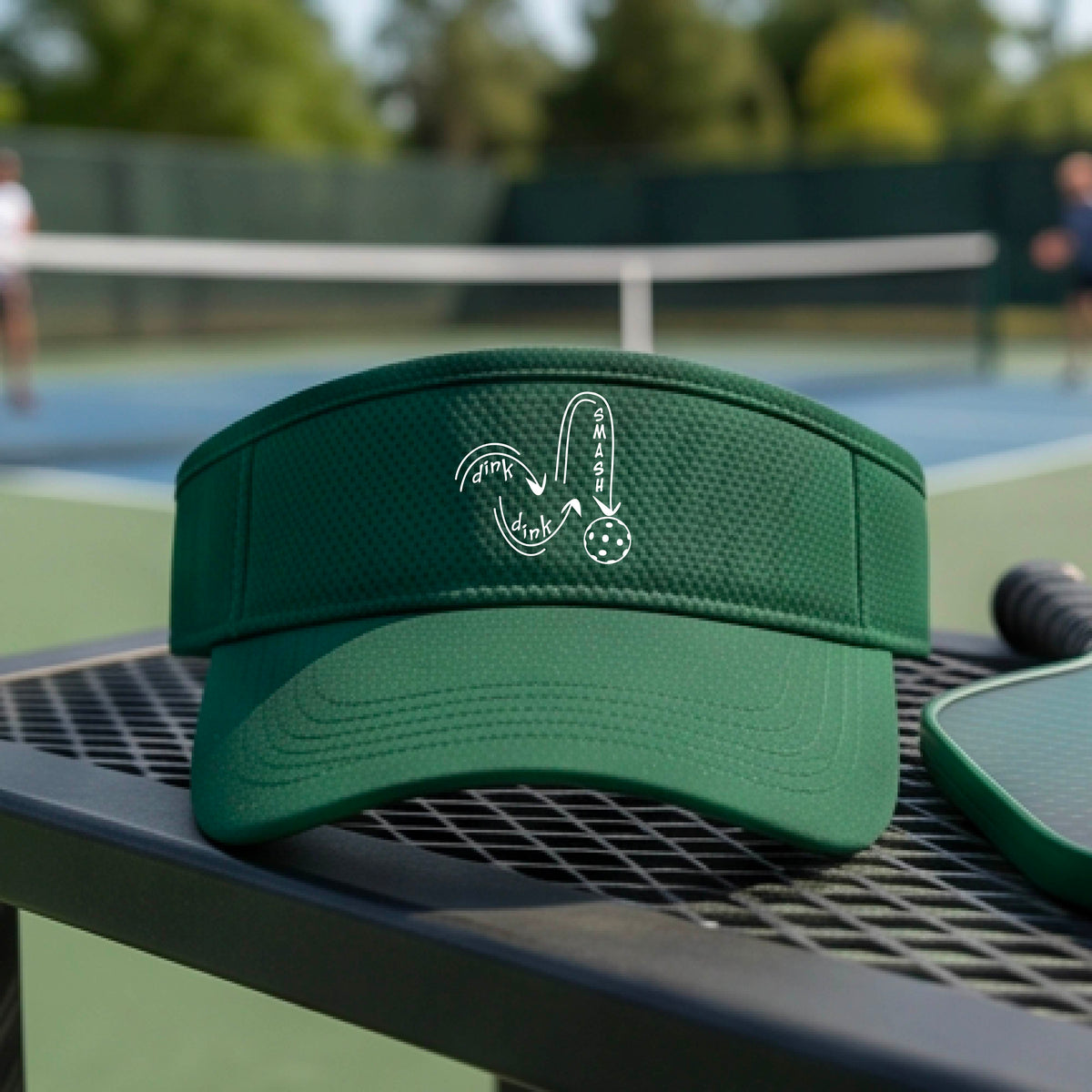 A close-up lifestyle shot of a green blue athletic visor with a white pickleball 'DINK DINK SMASH' logo with a pickleball graphic