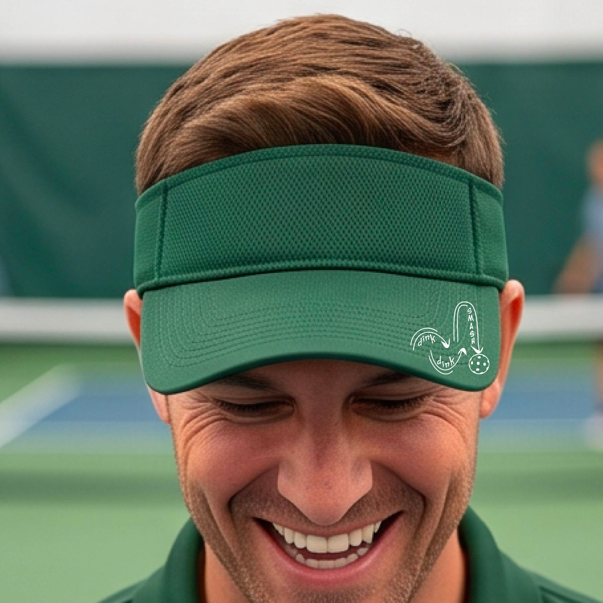 A close-up lifestyle shot of a green athletic visor with a white pickleball 'DINK DINK SMASH' logo with a pickleball graphic