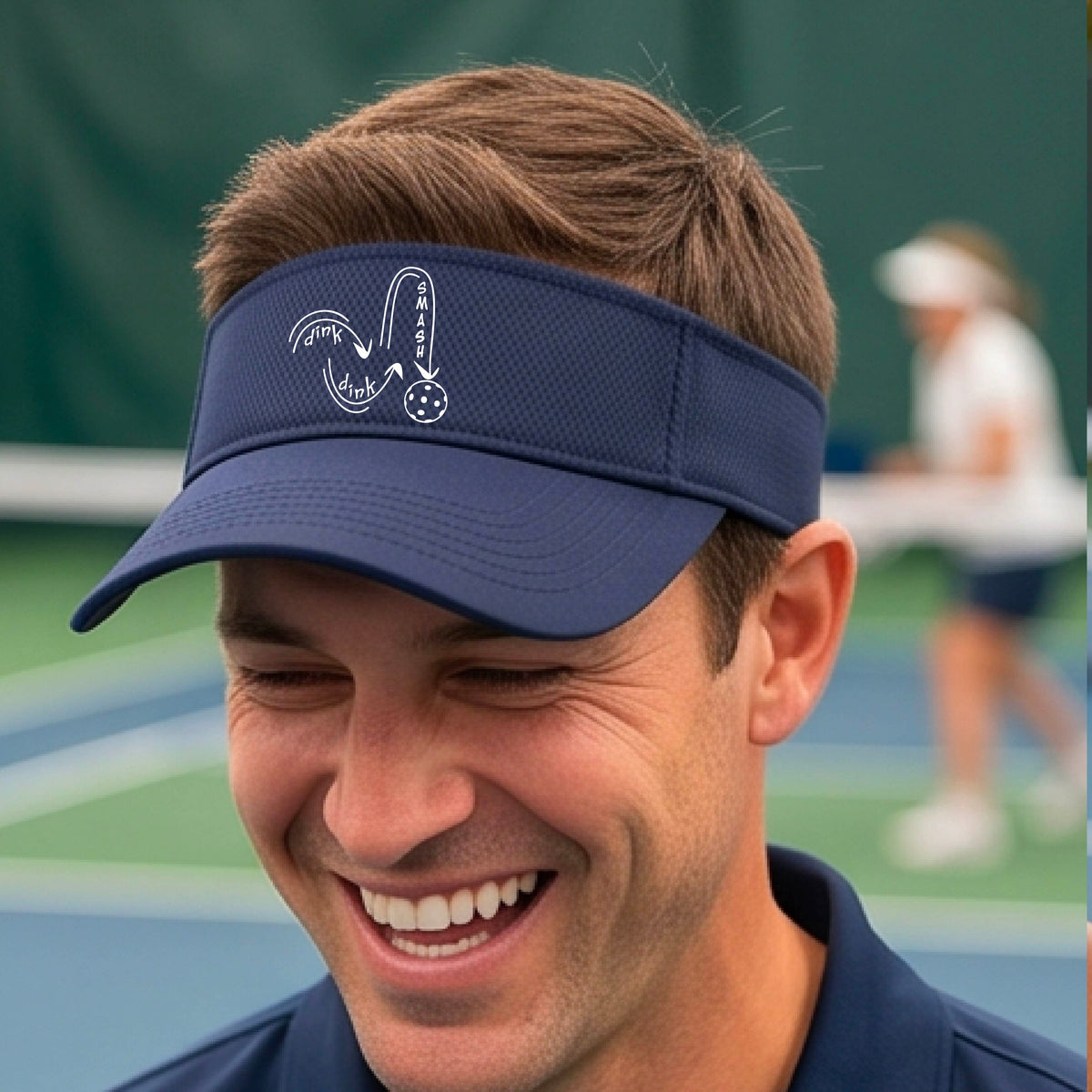 A close-up lifestyle shot of a navy blue athletic visor with a white pickleball 'DINK DINK SMASH' logo with a pickleball graphic