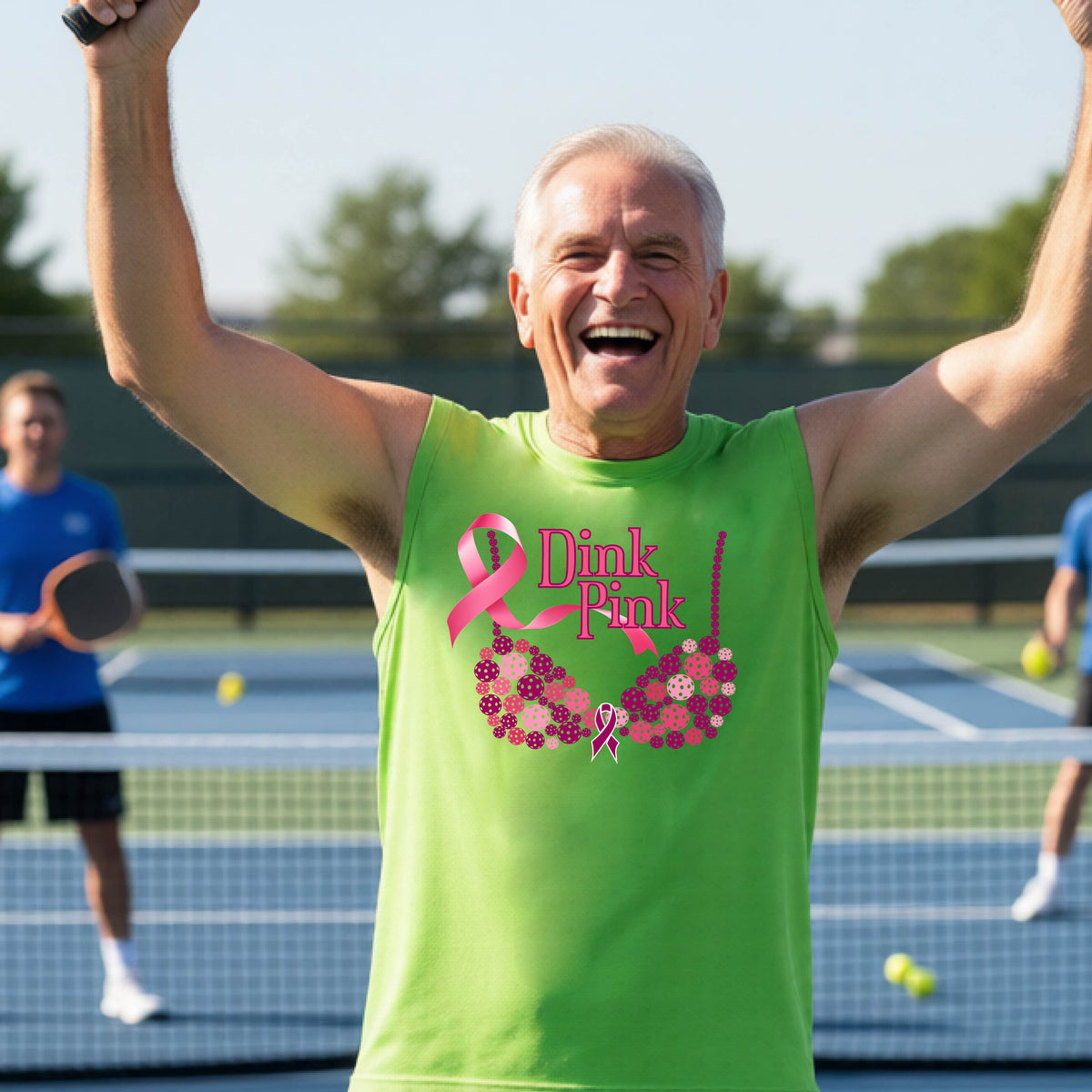 A smiling man wearing a lime green sleeveless tank top with a pink 'Dink Pink' breast cancer awareness graphic stands on an outdoor pickleball court. 