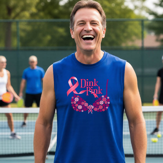 A smiling man wearing a blue sleeveless tank top with a pink 'Dink Pink' breast cancer awareness graphic stands on an outdoor pickleball court. 