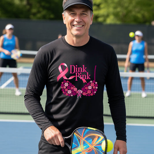 A smiling man wearing a black long-sleeve shirt with a pink 'Dink Pink' breast cancer awareness graphic stands on a pickleball court.