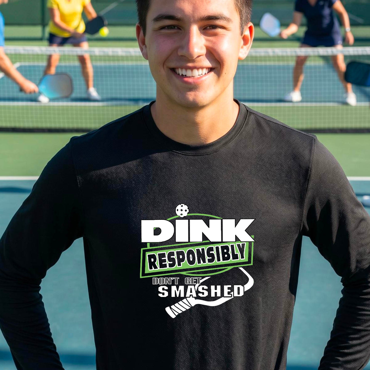 A man wearing a black long-sleeve t-shirt with a 'DINK RESPONSIBLY DON'T LET SMASHED' graphic on the front, and a pickelball paddle graphic.