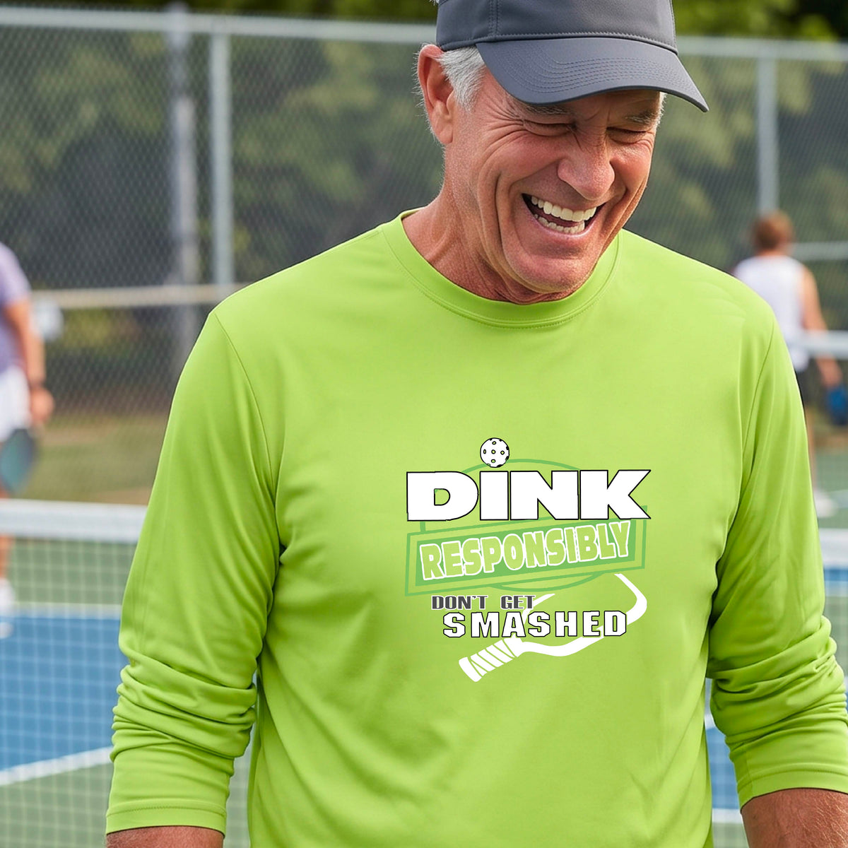 A man wearing a bright lime green long-sleeve t-shirt with a 'DINK RESPONSIBLY DON'T LET SMASHED' graphic on the front, and a pickelball paddle graphic.